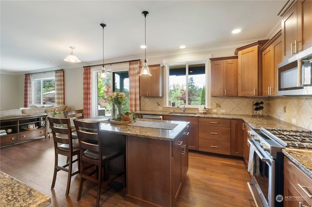 kitchen with a kitchen island, appliances with stainless steel finishes, a kitchen bar, hanging light fixtures, and ornamental molding