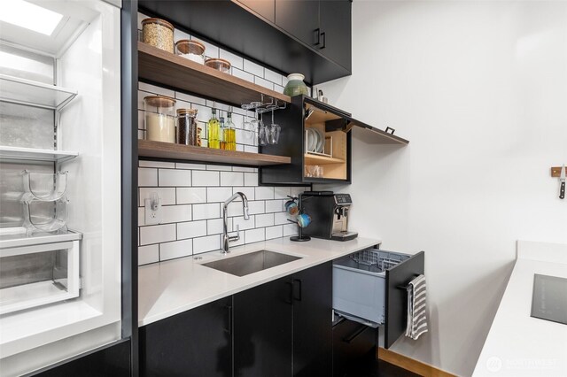 kitchen with decorative backsplash, dark cabinets, light countertops, open shelves, and a sink