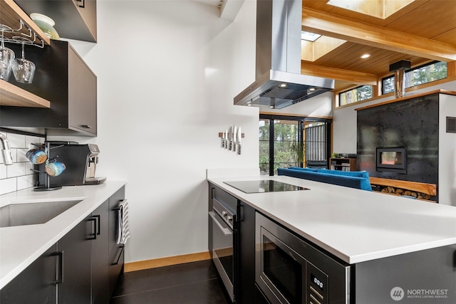 kitchen with tasteful backsplash, wall oven, island range hood, dark cabinets, and black electric cooktop