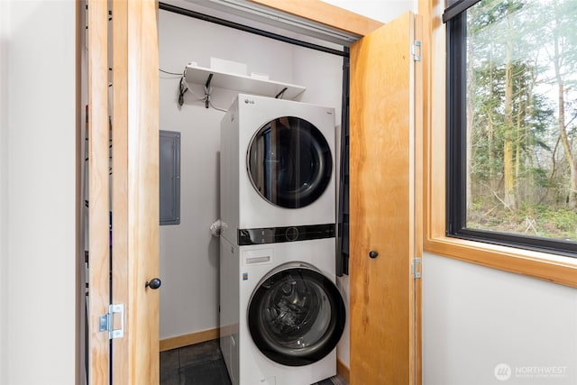 clothes washing area featuring laundry area, stacked washer / dryer, electric panel, and baseboards