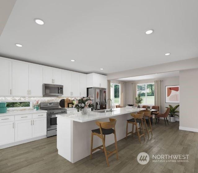 kitchen featuring a kitchen bar, dark hardwood / wood-style flooring, an island with sink, stainless steel appliances, and white cabinets