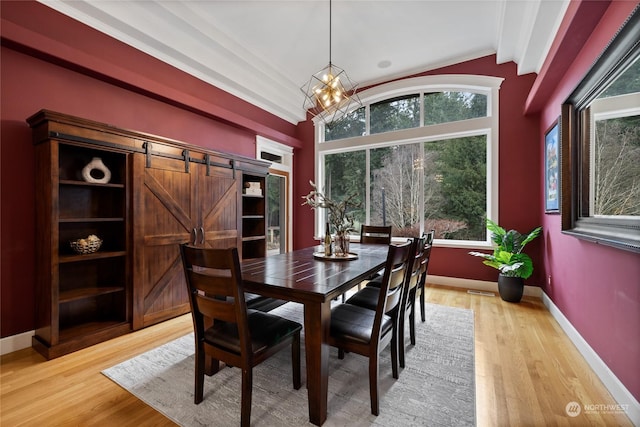 dining area featuring light wood-type flooring, a barn door, lofted ceiling with beams, and a notable chandelier