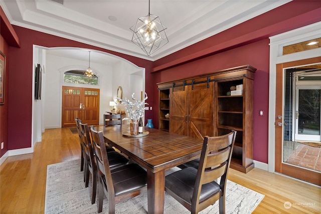 dining space featuring a barn door, ornamental molding, a tray ceiling, and light wood-type flooring