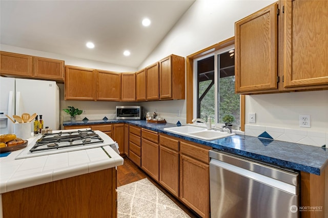 kitchen featuring lofted ceiling, sink, hardwood / wood-style flooring, tile counters, and stainless steel appliances