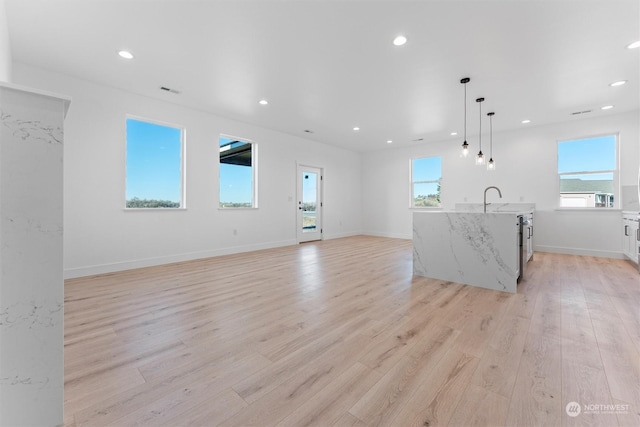 unfurnished living room with plenty of natural light, sink, and light wood-type flooring