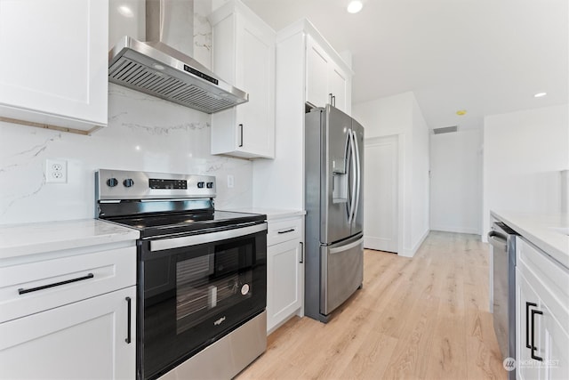 kitchen featuring wall chimney range hood, stainless steel appliances, white cabinets, and light wood-type flooring