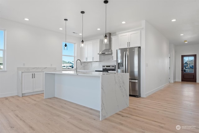 kitchen with pendant lighting, wall chimney range hood, appliances with stainless steel finishes, white cabinetry, and decorative backsplash