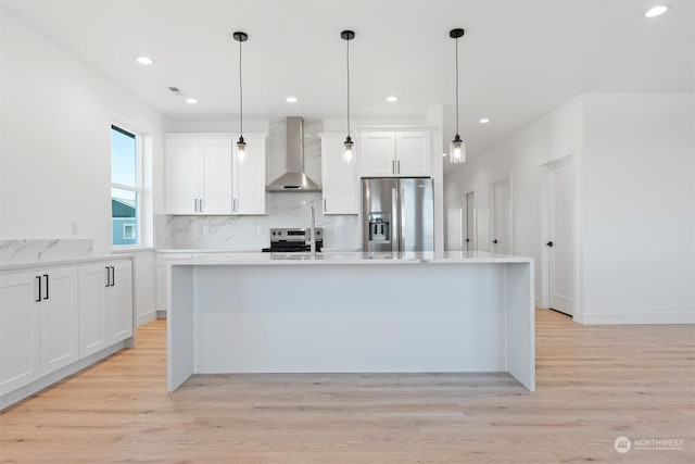 kitchen with stainless steel appliances, a kitchen island with sink, wall chimney range hood, and white cabinets