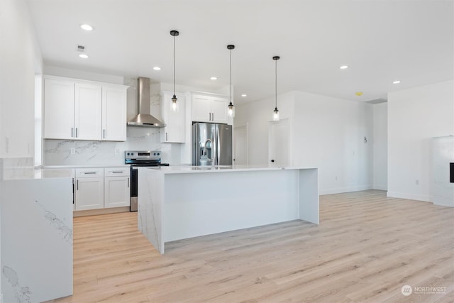 kitchen featuring appliances with stainless steel finishes, decorative light fixtures, white cabinetry, backsplash, and wall chimney exhaust hood