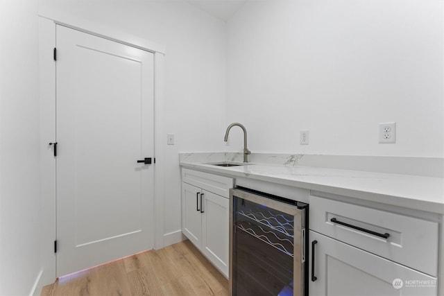 bar with white cabinetry, sink, beverage cooler, light hardwood / wood-style floors, and light stone countertops