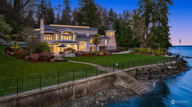 back house at dusk with a lawn and a water view