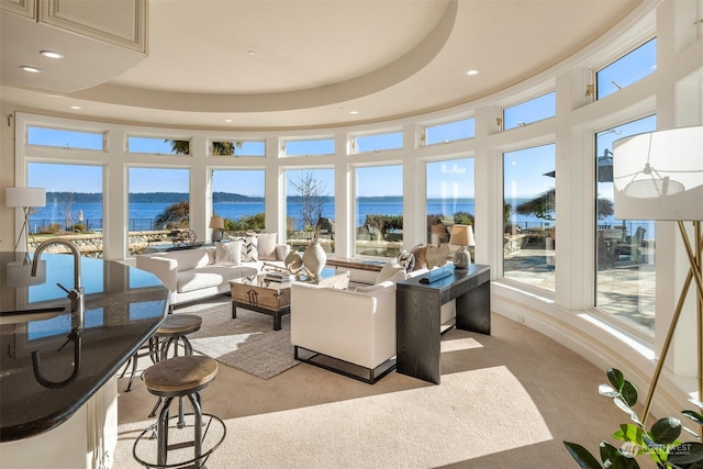 carpeted living room featuring a high ceiling, a raised ceiling, a water view, and sink