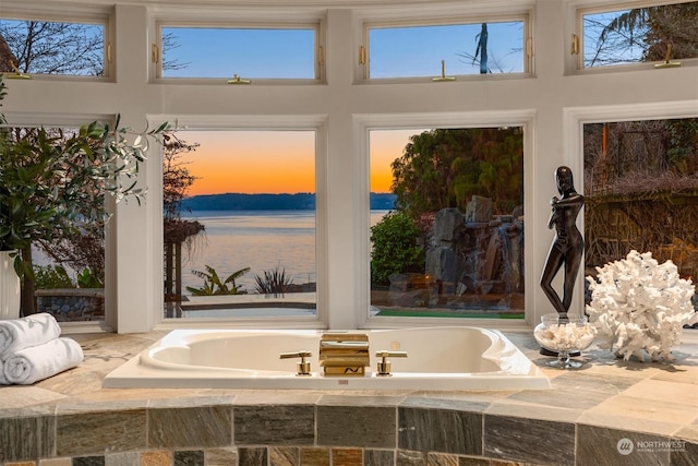 interior space with tiled bath and a water view