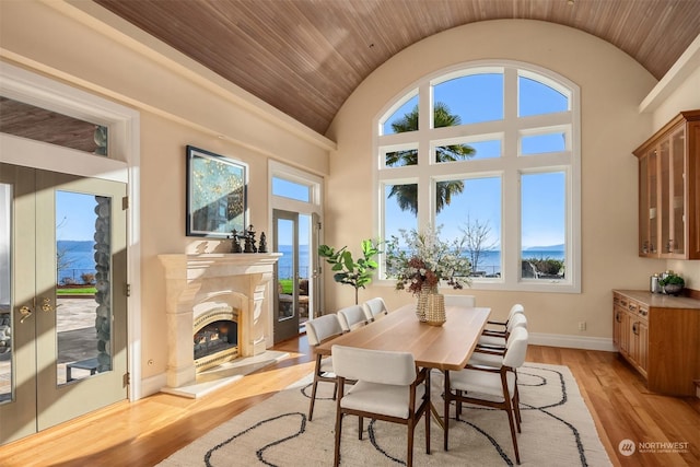 dining room featuring a water view, a premium fireplace, lofted ceiling, and light wood-type flooring