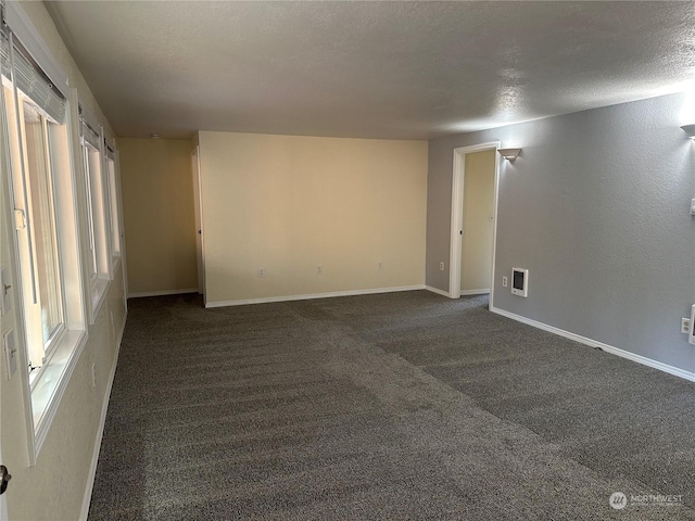 spare room with a textured ceiling and dark colored carpet