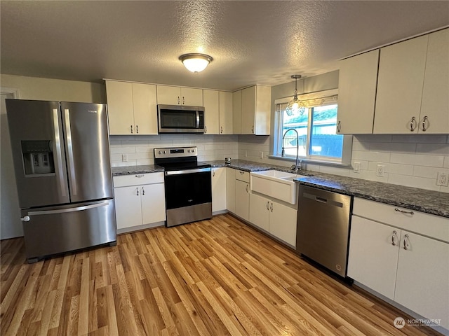 kitchen with decorative light fixtures, white cabinetry, sink, stainless steel appliances, and light hardwood / wood-style flooring