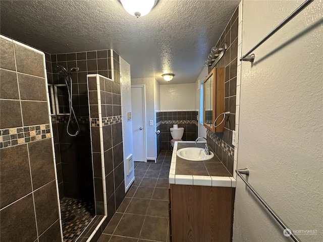 bathroom with a tile shower, tile walls, vanity, tile patterned floors, and a textured ceiling