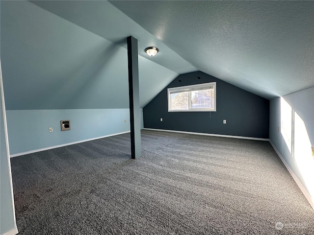 additional living space with dark carpet, vaulted ceiling, and a textured ceiling