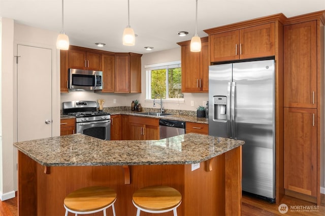 kitchen featuring light stone countertops, pendant lighting, brown cabinets, appliances with stainless steel finishes, and a sink