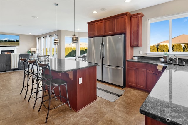 kitchen featuring sink, hanging light fixtures, stainless steel refrigerator, a kitchen island, and dark stone counters