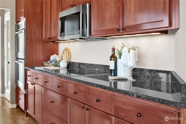 kitchen featuring light tile patterned floors, stainless steel appliances, and dark stone counters