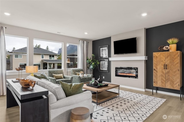 living area with a glass covered fireplace, light wood-type flooring, and recessed lighting