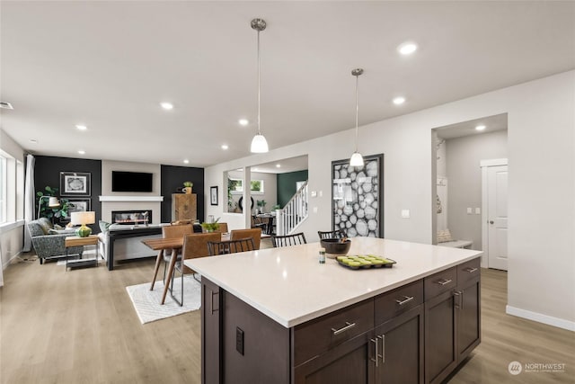 kitchen featuring pendant lighting, a glass covered fireplace, a kitchen island, light wood-style floors, and light countertops