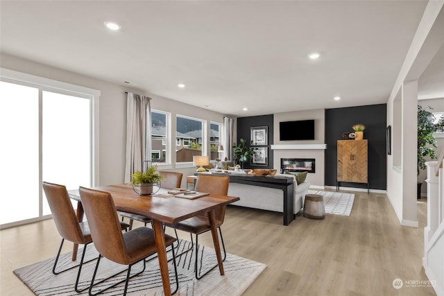 dining area with light wood-style floors, recessed lighting, and a glass covered fireplace