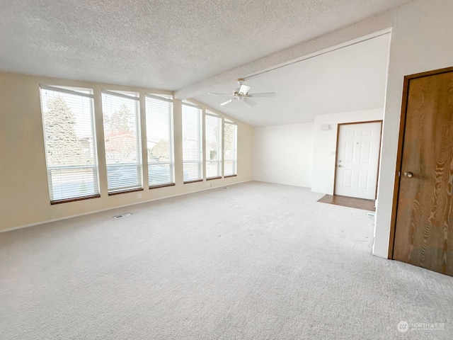 carpeted empty room with plenty of natural light, vaulted ceiling with beams, and a textured ceiling