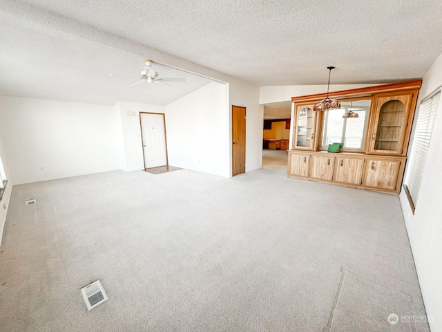 unfurnished living room with vaulted ceiling, light colored carpet, a textured ceiling, and ceiling fan