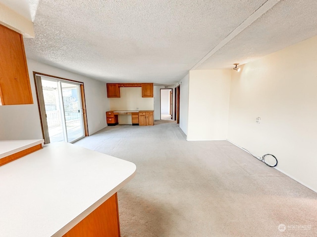 unfurnished living room featuring light colored carpet, built in desk, and a textured ceiling