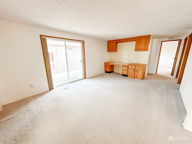 unfurnished living room featuring light carpet, built in desk, and a textured ceiling