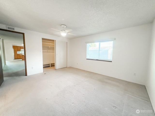 unfurnished bedroom with ceiling fan, baseboard heating, a textured ceiling, light carpet, and a closet