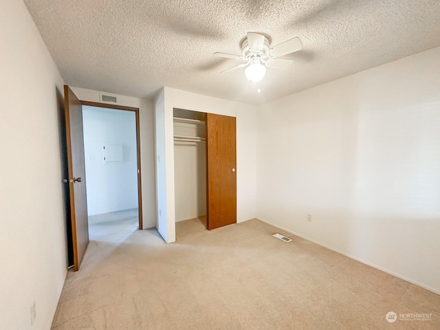 unfurnished bedroom featuring light carpet, a textured ceiling, ceiling fan, and a closet