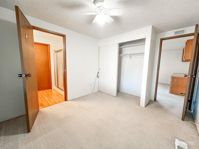 unfurnished bedroom with ceiling fan, light colored carpet, a textured ceiling, and a closet