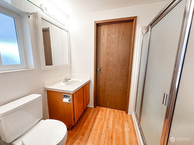 bathroom featuring a shower with door, vanity, wood-type flooring, and toilet