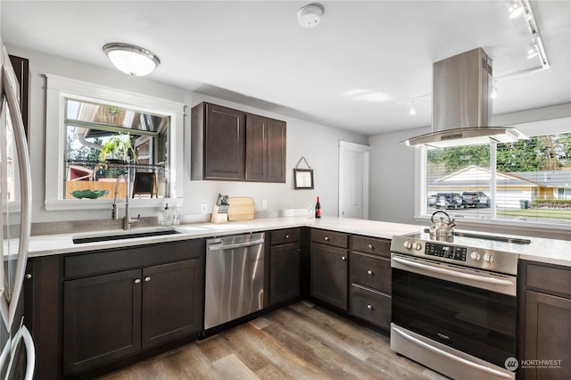 kitchen featuring sink, dark brown cabinets, appliances with stainless steel finishes, island exhaust hood, and light hardwood / wood-style floors