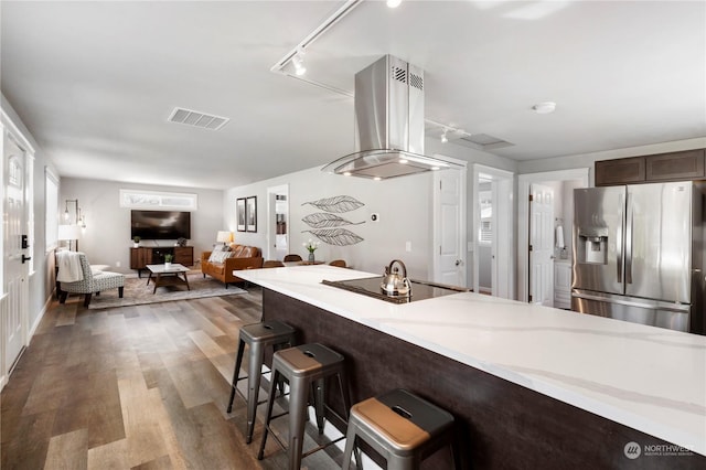 kitchen with stainless steel refrigerator with ice dispenser, a breakfast bar area, island range hood, dark hardwood / wood-style flooring, and black electric stovetop