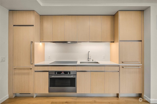 kitchen with stainless steel oven, black electric stovetop, light brown cabinetry, and sink