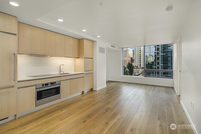 kitchen with light brown cabinetry, sink, light hardwood / wood-style floors, and stainless steel oven