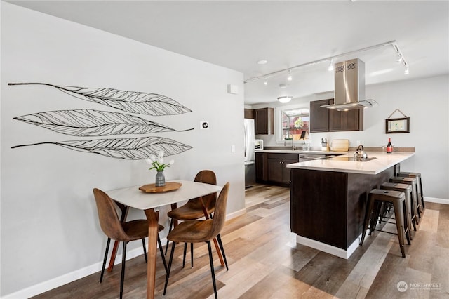 kitchen featuring light hardwood / wood-style flooring, a breakfast bar, dark brown cabinetry, island exhaust hood, and kitchen peninsula