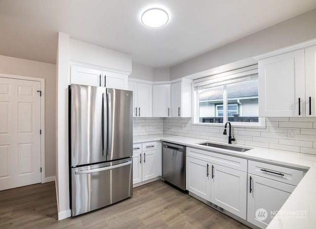 kitchen with sink, tasteful backsplash, light wood-type flooring, appliances with stainless steel finishes, and white cabinets