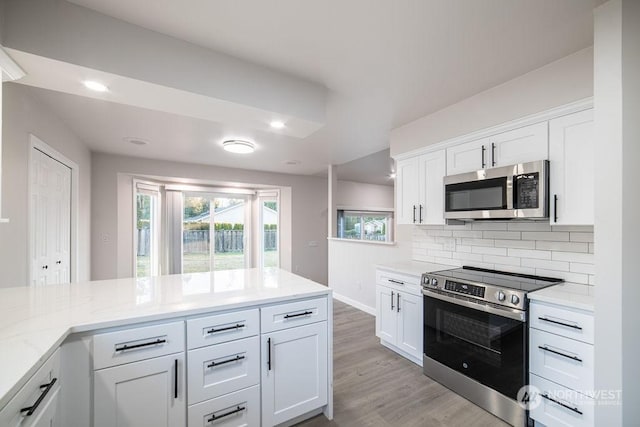 kitchen featuring appliances with stainless steel finishes, white cabinets, decorative backsplash, light stone counters, and light hardwood / wood-style flooring