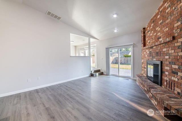 unfurnished living room with hardwood / wood-style flooring, a brick fireplace, and lofted ceiling