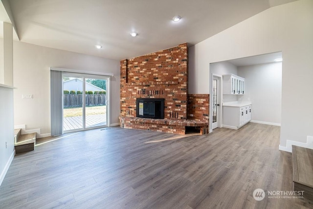 unfurnished living room with vaulted ceiling, a fireplace, and light hardwood / wood-style flooring