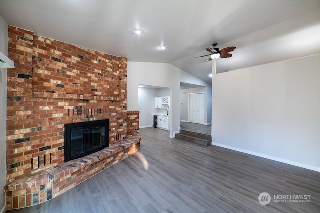 unfurnished living room featuring dark hardwood / wood-style flooring, a brick fireplace, vaulted ceiling, and ceiling fan