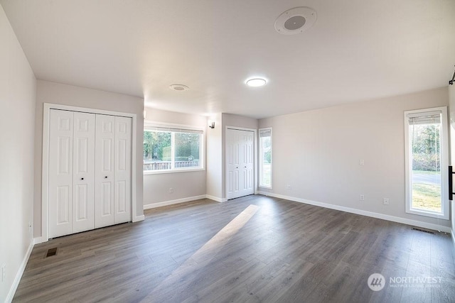 unfurnished bedroom with dark wood-type flooring and two closets