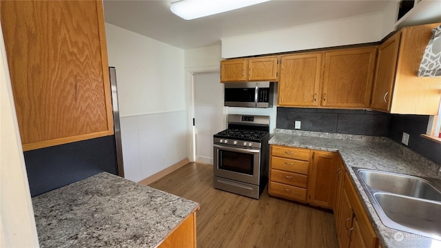 kitchen with sink, appliances with stainless steel finishes, backsplash, light stone counters, and wood-type flooring