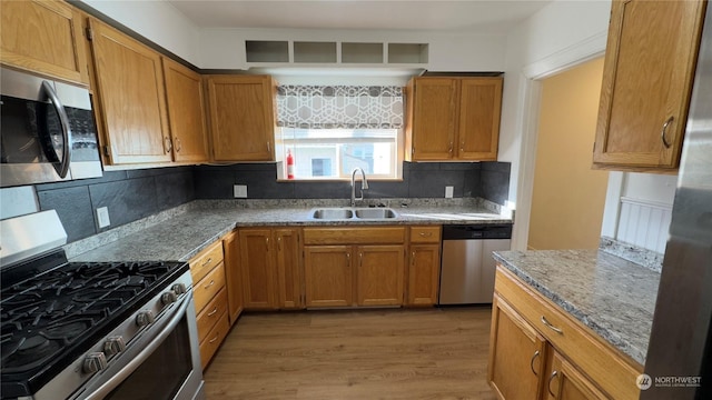 kitchen featuring sink, appliances with stainless steel finishes, backsplash, hardwood / wood-style floors, and stone countertops