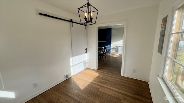 unfurnished dining area featuring an inviting chandelier, a barn door, and dark hardwood / wood-style flooring